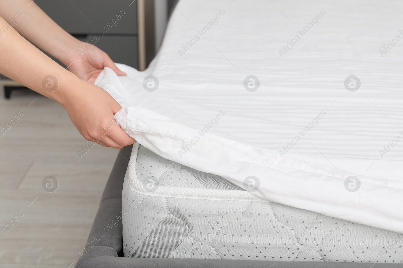 Photo of Woman putting cover on mattress indoors, closeup