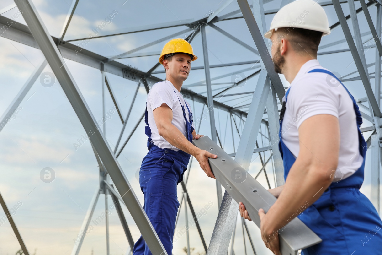 Photo of Workers building high voltage tower construction outdoors. Installation of electrical substation