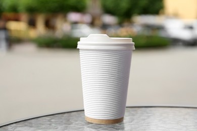 Photo of Paper cup of coffee on table outdoors, closeup. Takeaway drink