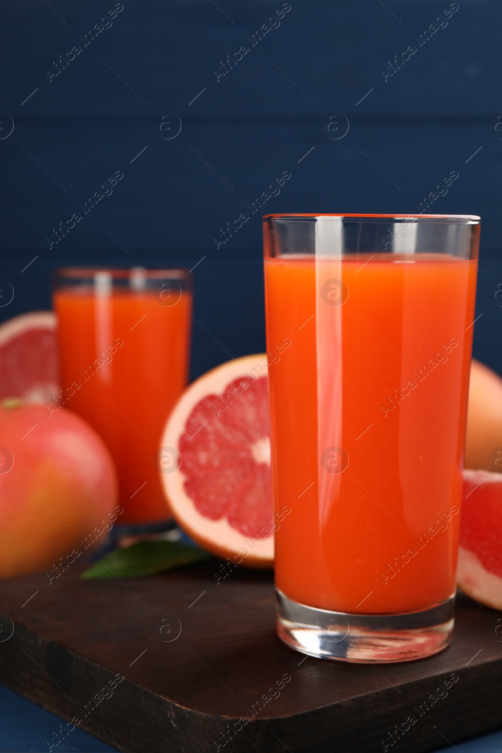 Photo of Tasty grapefruit juice in glass and fresh fruits on table, closeup