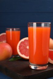 Photo of Tasty grapefruit juice in glass and fresh fruits on table, closeup