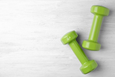 Photo of Bright dumbbells and space for text on wooden background, flat lay. Home fitness