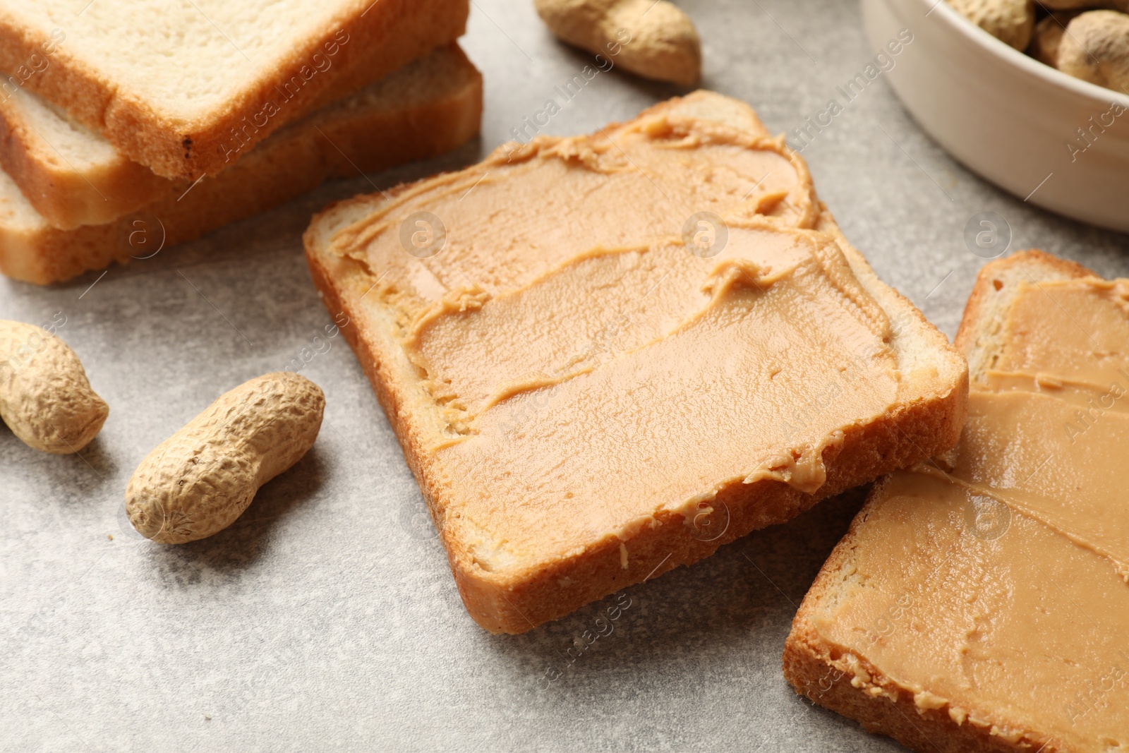 Photo of Tasty peanut butter sandwiches and peanuts on gray table, closeup