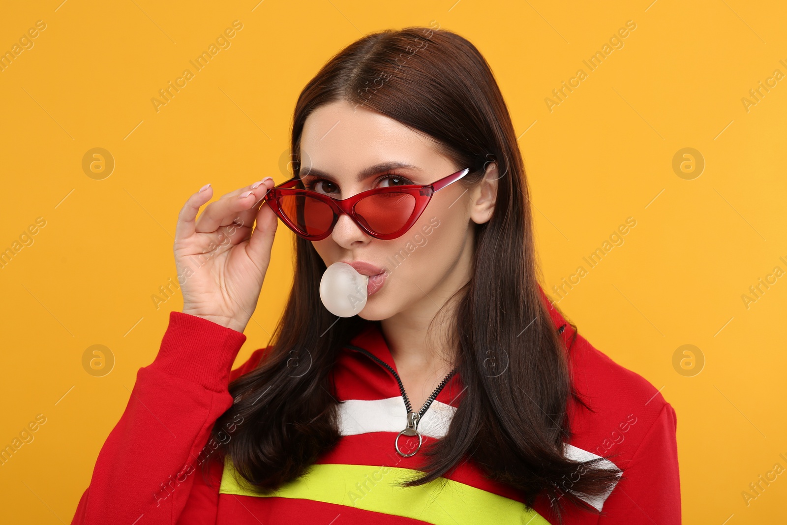 Photo of Beautiful woman in sunglasses blowing bubble gum on orange background