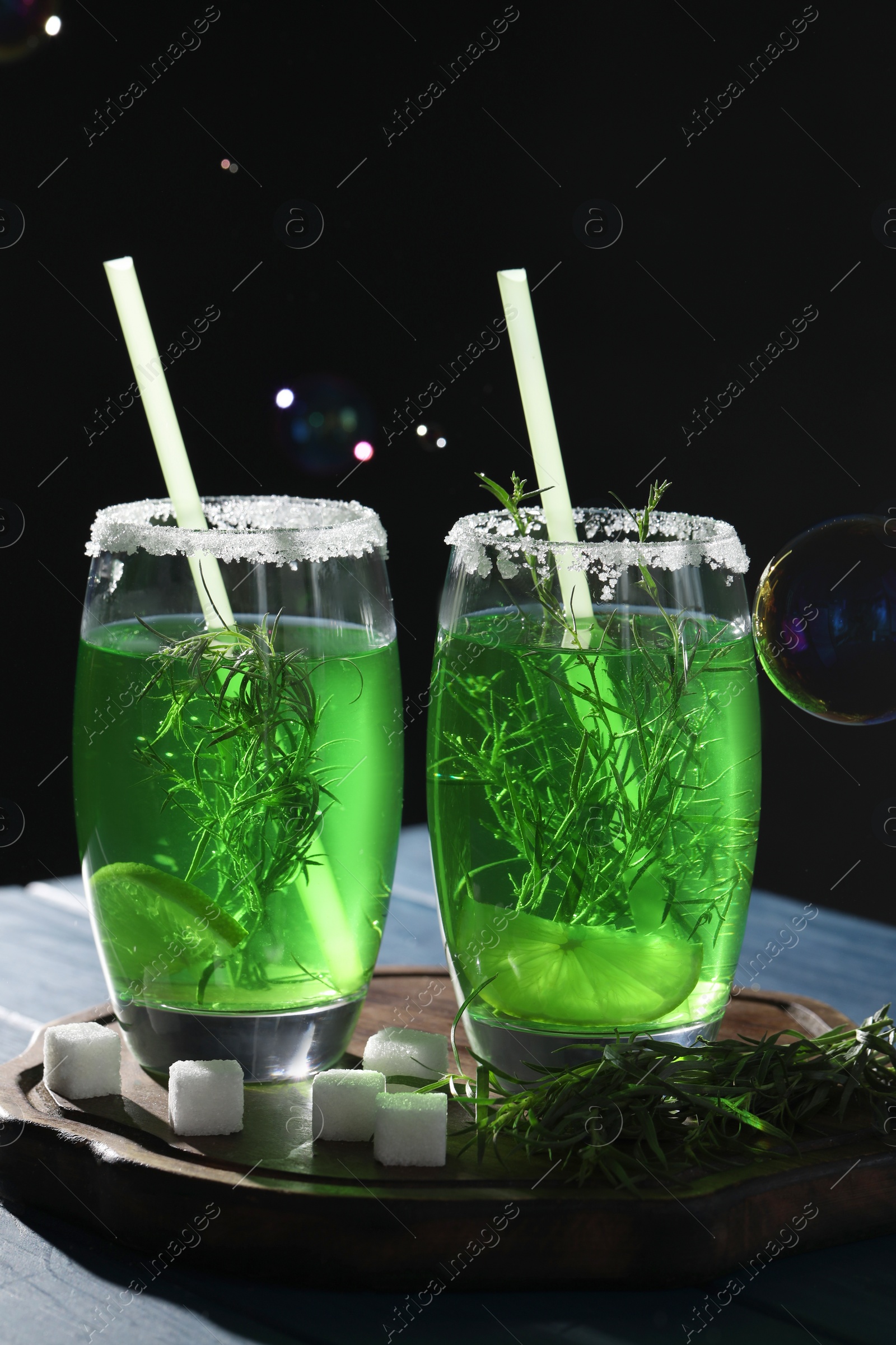 Photo of Glasses of homemade refreshing tarragon drink, sprigs and sugar cubes on table