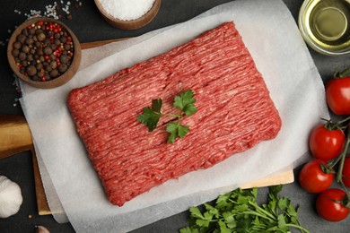 Raw fresh minced meat, tomatoes and other ingredients on black table, flat lay