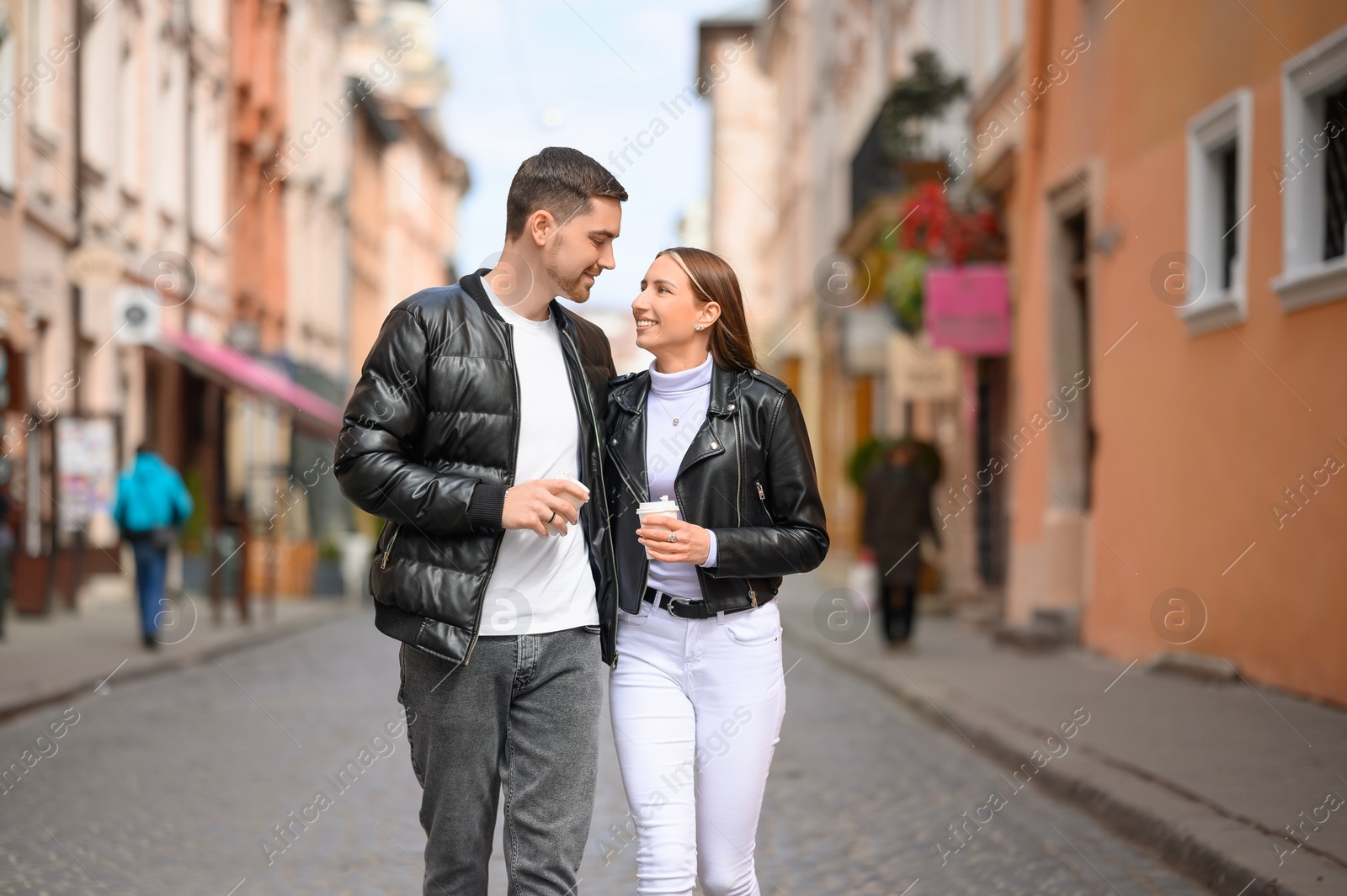 Photo of Lovely young couple with cups of coffee walking together on city street. Romantic date