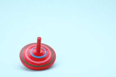 Photo of One bright spinning top on light blue background, space for text. Toy whirligig