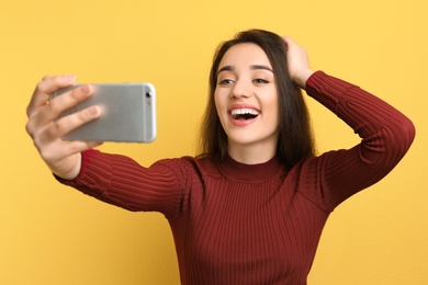 Photo of Attractive young woman taking selfie with phone on color background