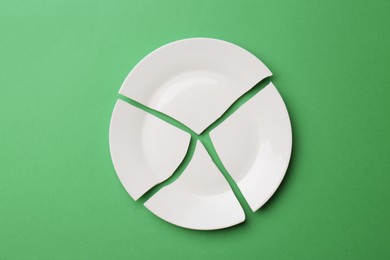 Photo of Pieces of broken ceramic plate on green background, flat lay