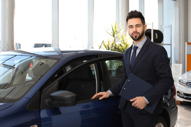 Photo of Young salesman with clipboard near car in dealership