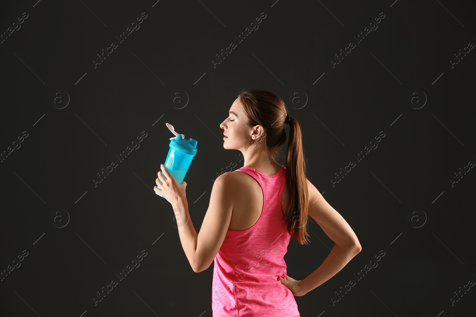 Photo of Athletic young woman drinking protein shake on black background