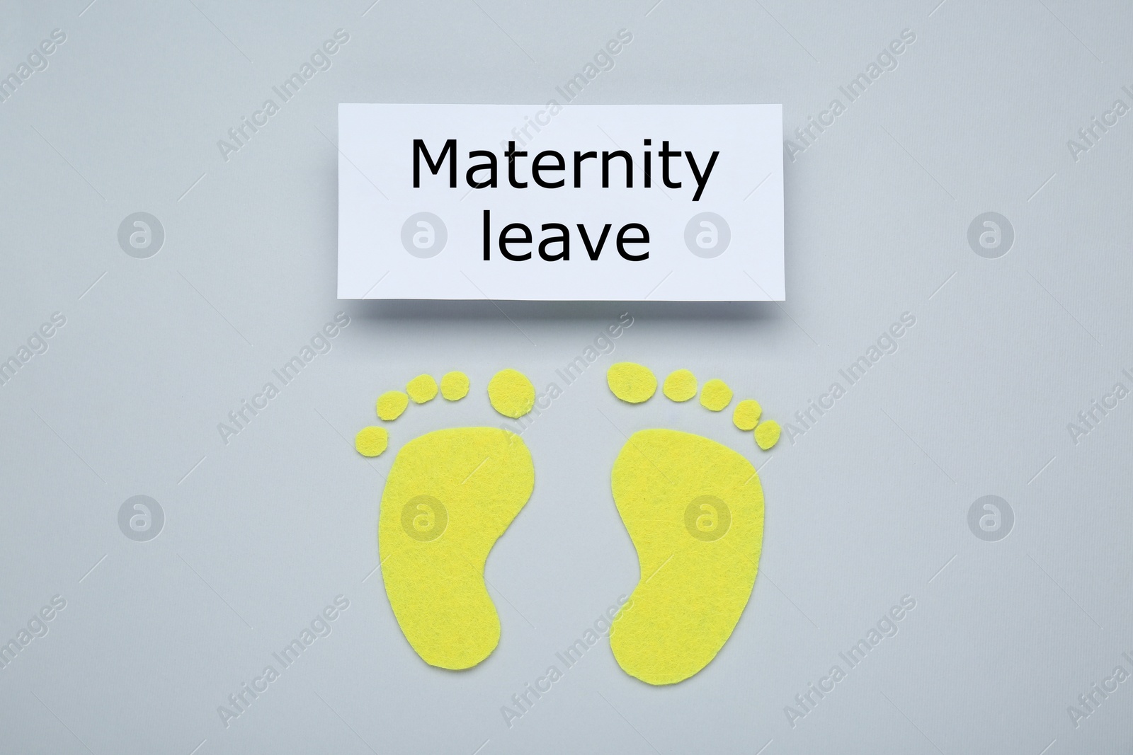 Photo of Note with words Maternity Leave and paper cutout of feet on light grey background, flat lay