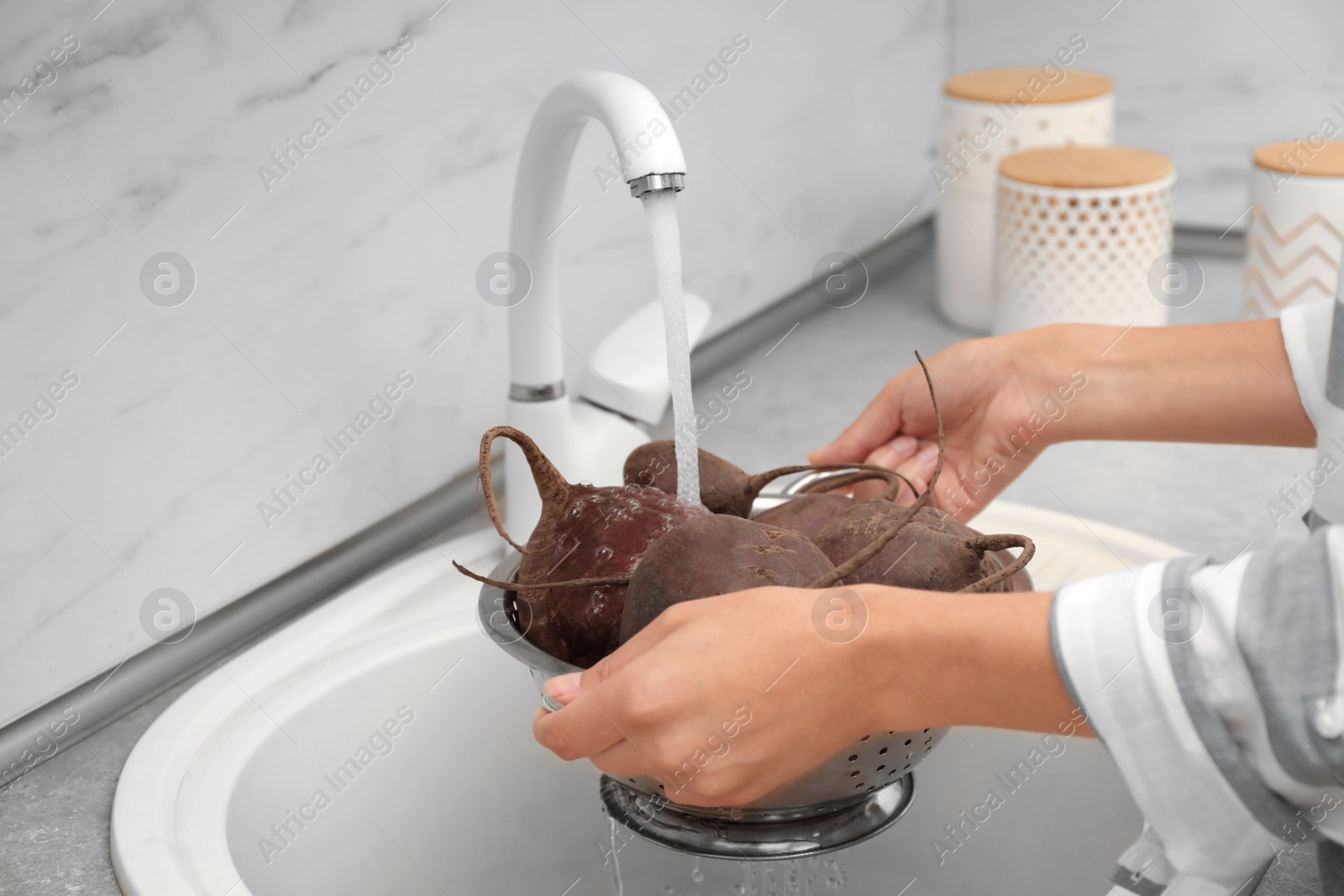 Photo of Woman washing ripe beets in kitchen sink, closeup