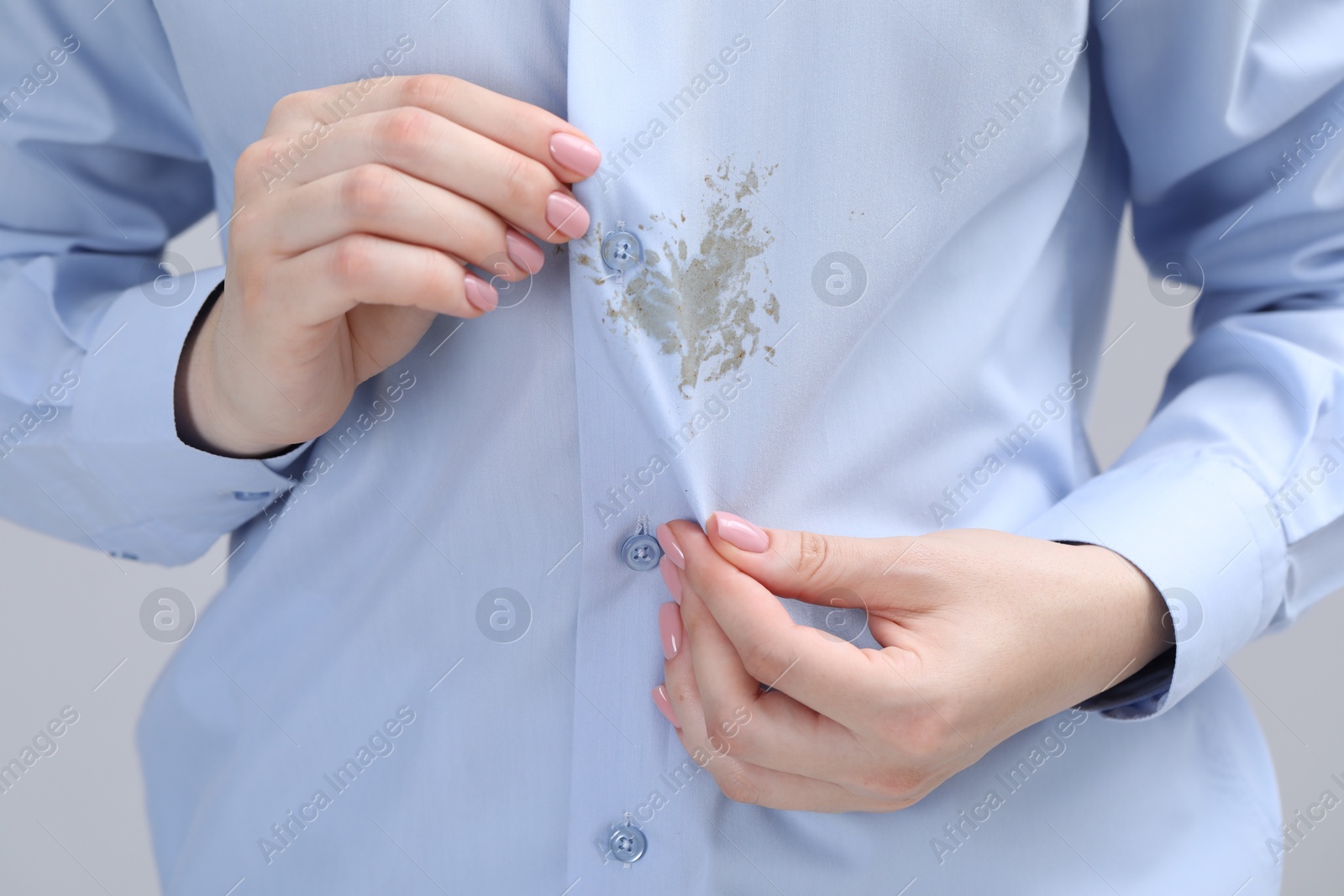 Photo of Woman showing stain on her shirt against light grey background, closeup