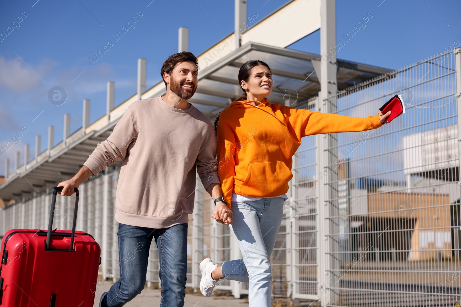 Photo of Being late. Couple with red suitcase running outdoors