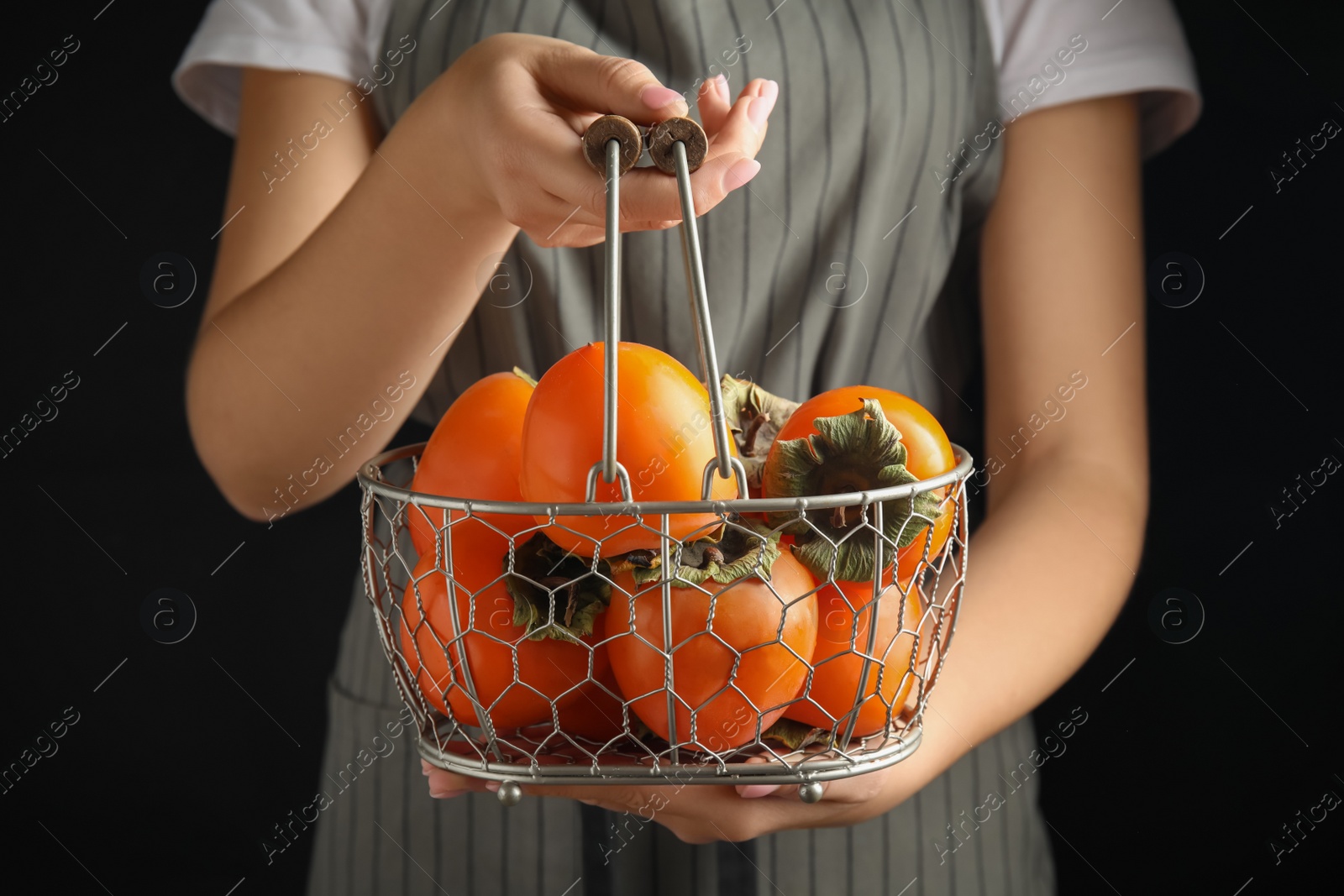 Photo of Woman holding delicious fresh persimmons on black background, closeup