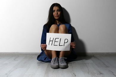 Abused young woman with sign HELP near white wall. Domestic violence concept