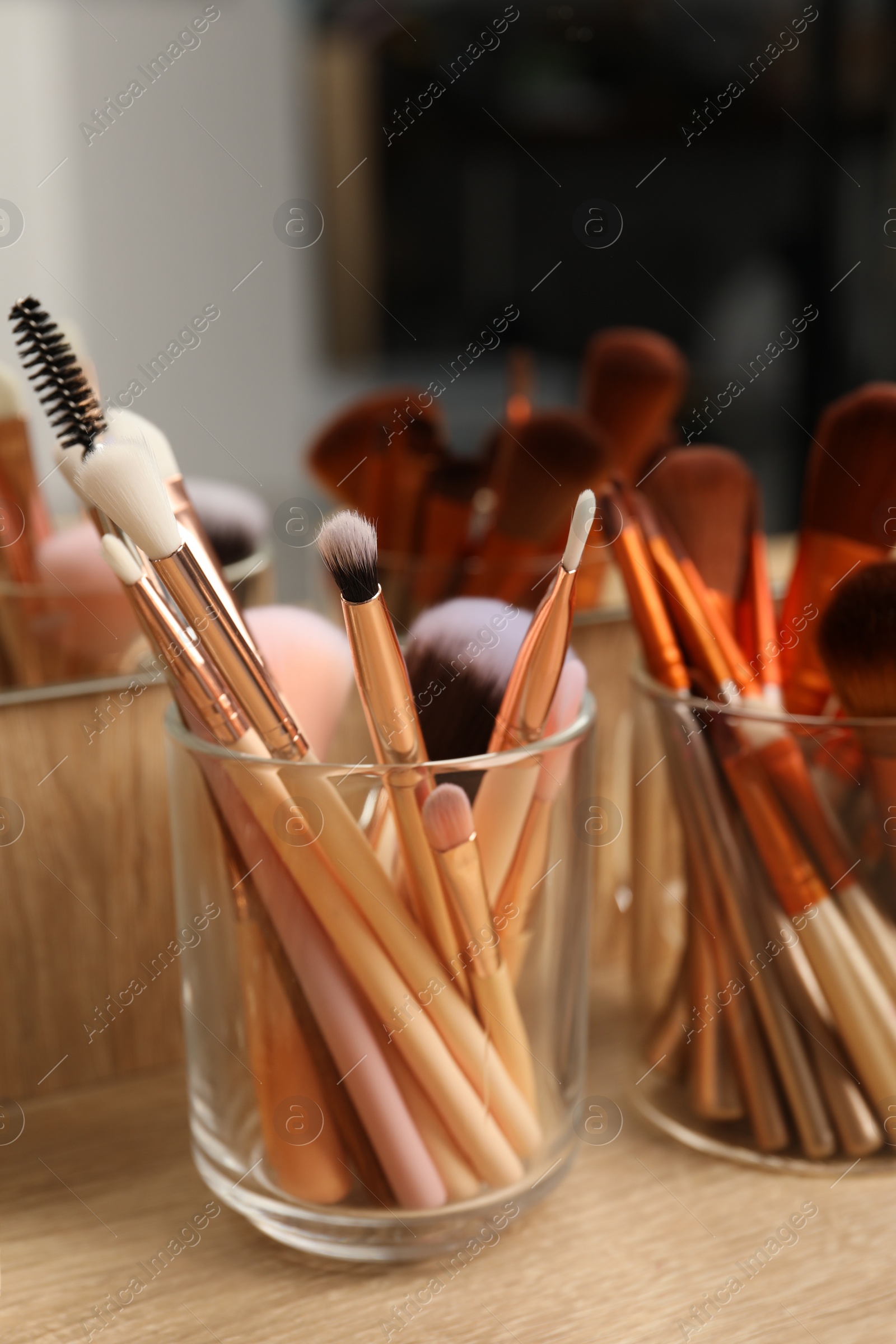 Photo of Set of professional makeup brushes near mirror on wooden table, closeup