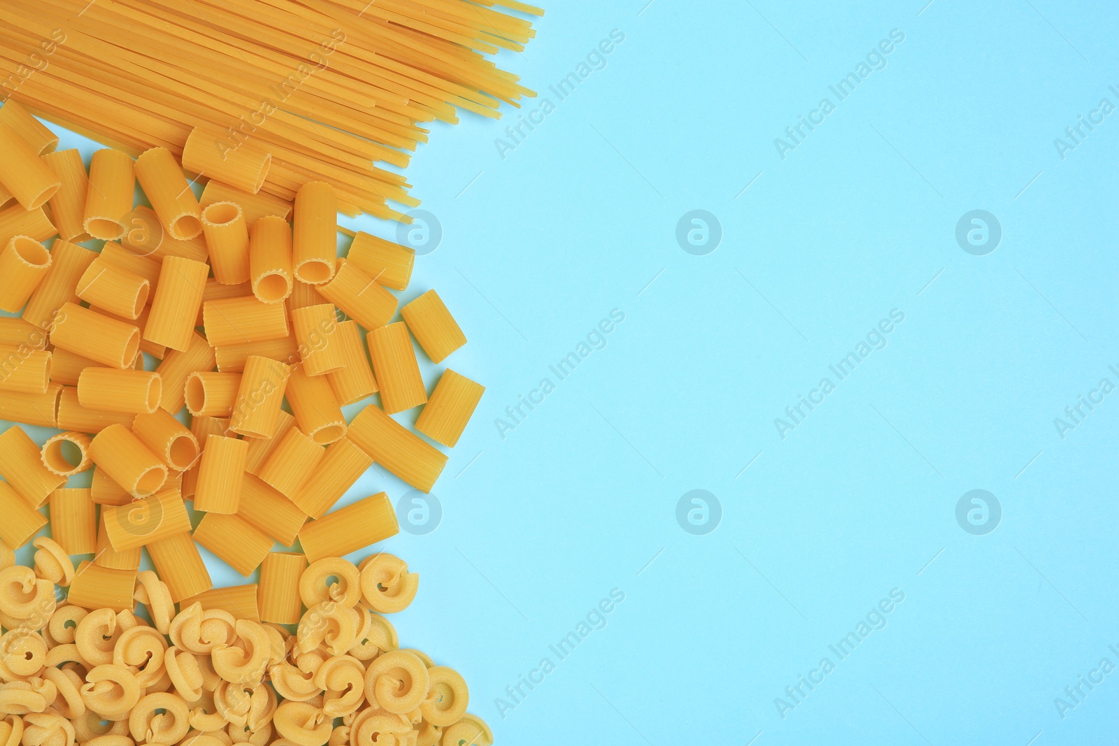 Photo of Different types of pasta on light blue background, flat lay. Space for text