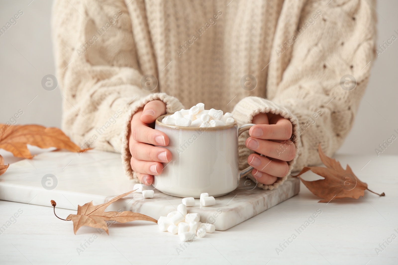 Photo of Woman in autumn sweater holding hot cozy drink at table