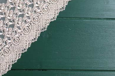 Beige lace on green wooden table, top view. Space for text