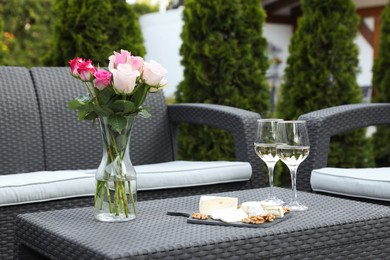 Photo of Vase with roses, glasses of wine and food on rattan table on outdoor terrace