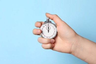 Woman holding vintage timer on light blue background, closeup. Space for text