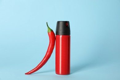 Photo of Bottle of gas spray and fresh chili pepper on light blue background
