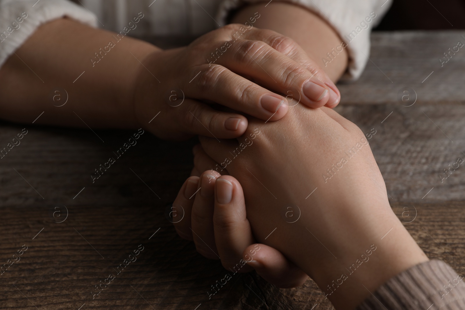 Photo of Woman holding hands with her mother at wooden table, closeup