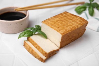 Photo of Delicious smoked tofu, soy sauce and basil on tiled table