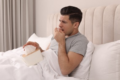 Photo of Sick man with box of paper tissues suffering from cold in bed at home