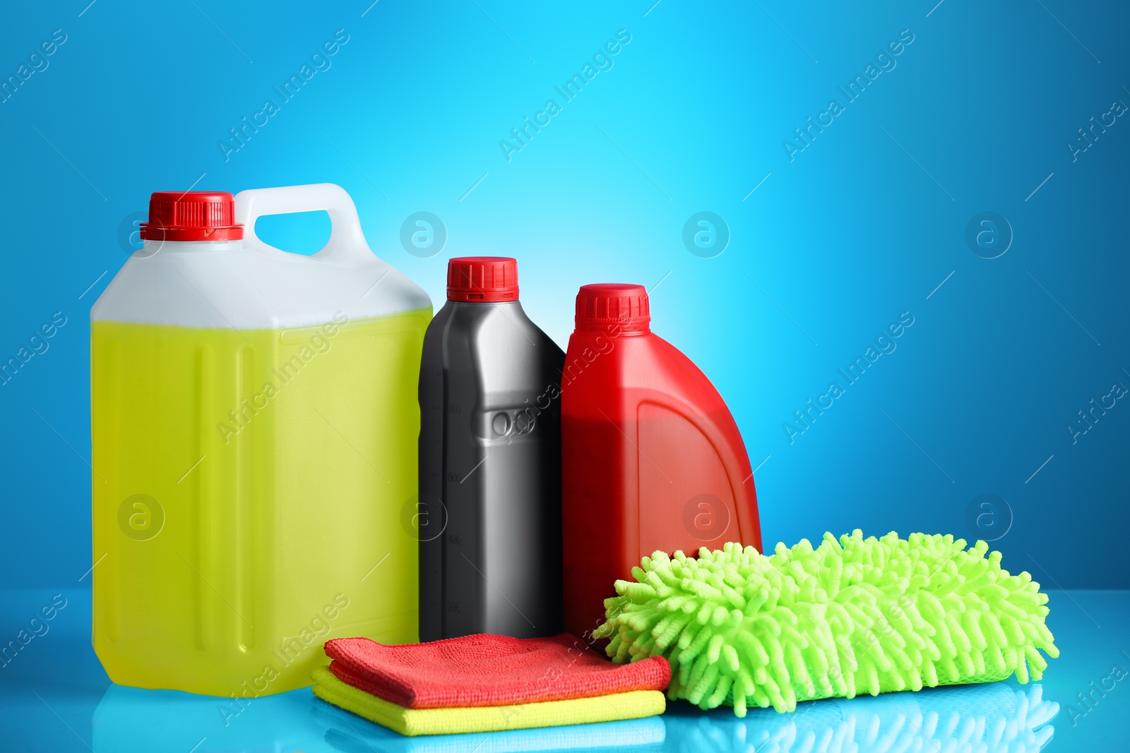 Photo of Bottles, stack of cloths and car wash mitt on light blue background