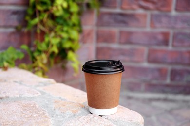 Photo of Disposable paper cup with plastic lid on stone parapet outdoors