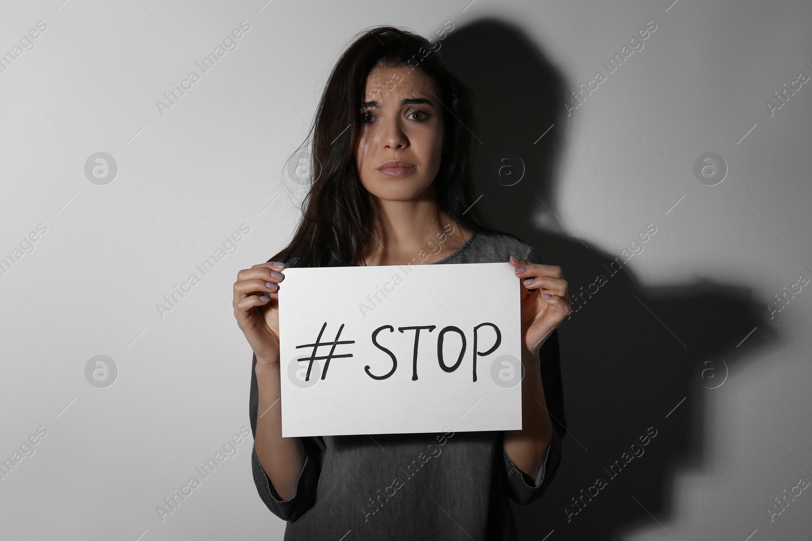 Photo of Abused young woman with hashtag STOP near white wall. Domestic violence concept