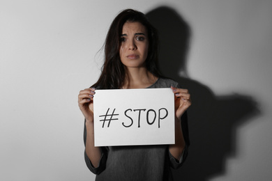 Abused young woman with hashtag STOP near white wall. Domestic violence concept