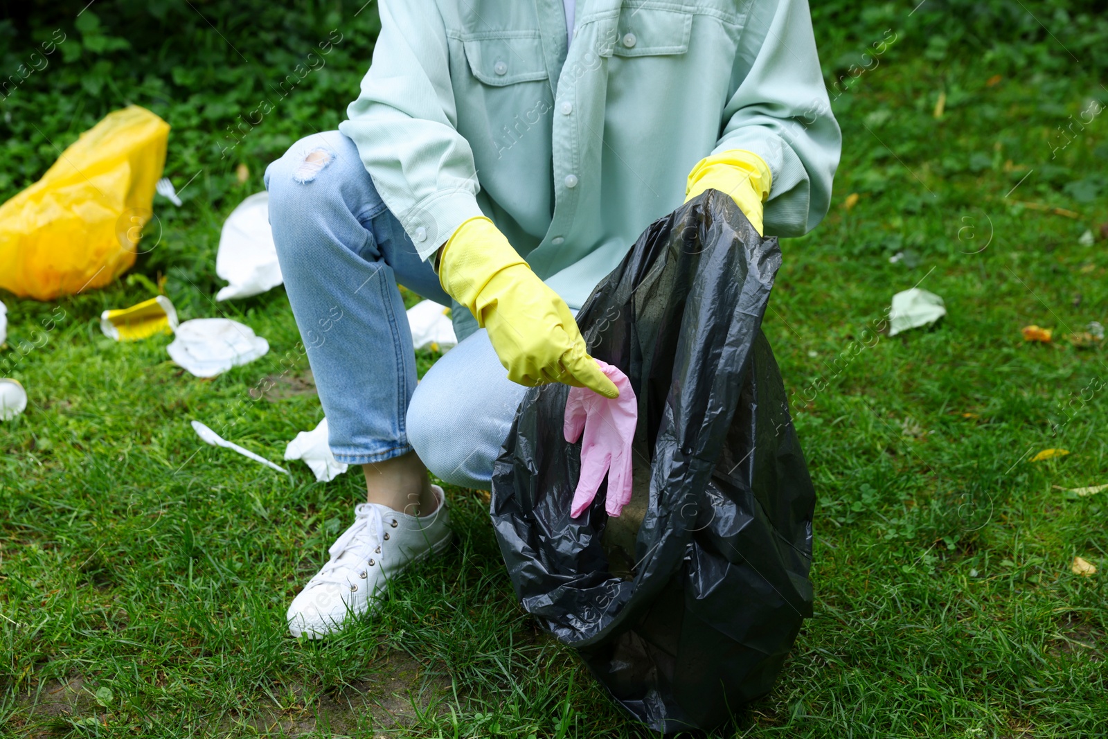 Photo of Woman with plastic bag collecting garbage on green grass outdoors, closeup