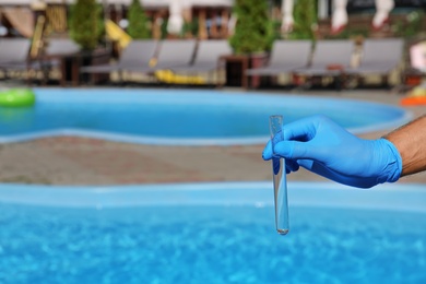 Man holding test tube with water against swimming pool on sunny day. Space for text
