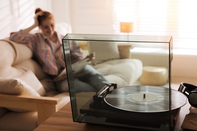 Photo of Young woman with vinyl discs in living room, focus on turntable