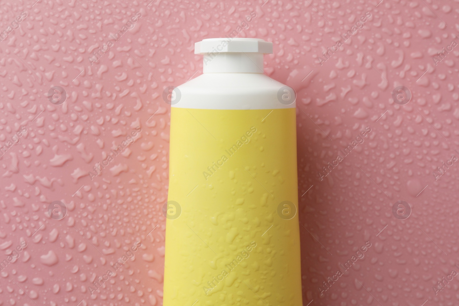 Photo of Moisturizing cream in tube on pink background with water drops, top view