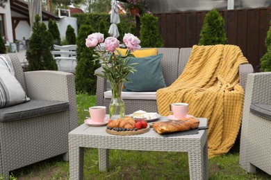 Photo of Morning drink, pastry, berries, cheese and vase with flowers on rattan table. Summer breakfast outdoors