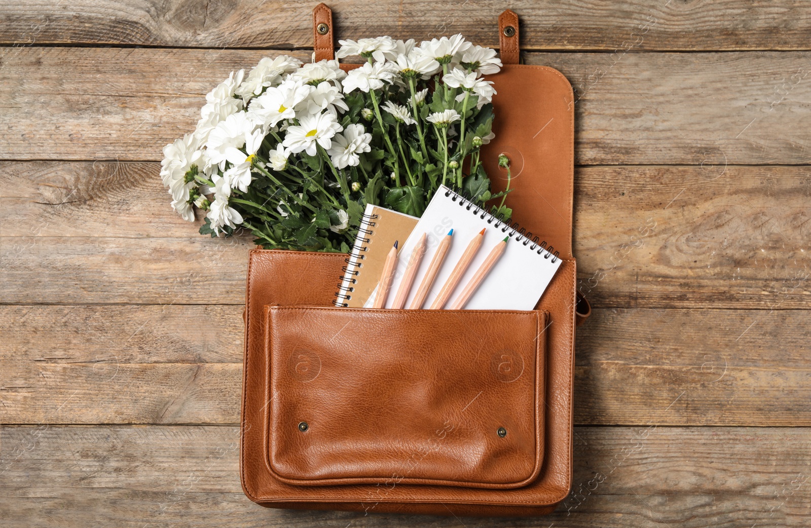 Photo of Leather briefcase with stationery and flowers on wooden table, top view. Teacher's Day