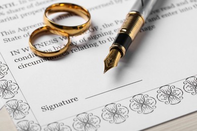 Photo of Marriage contract, gold rings and pen on light wooden table, closeup