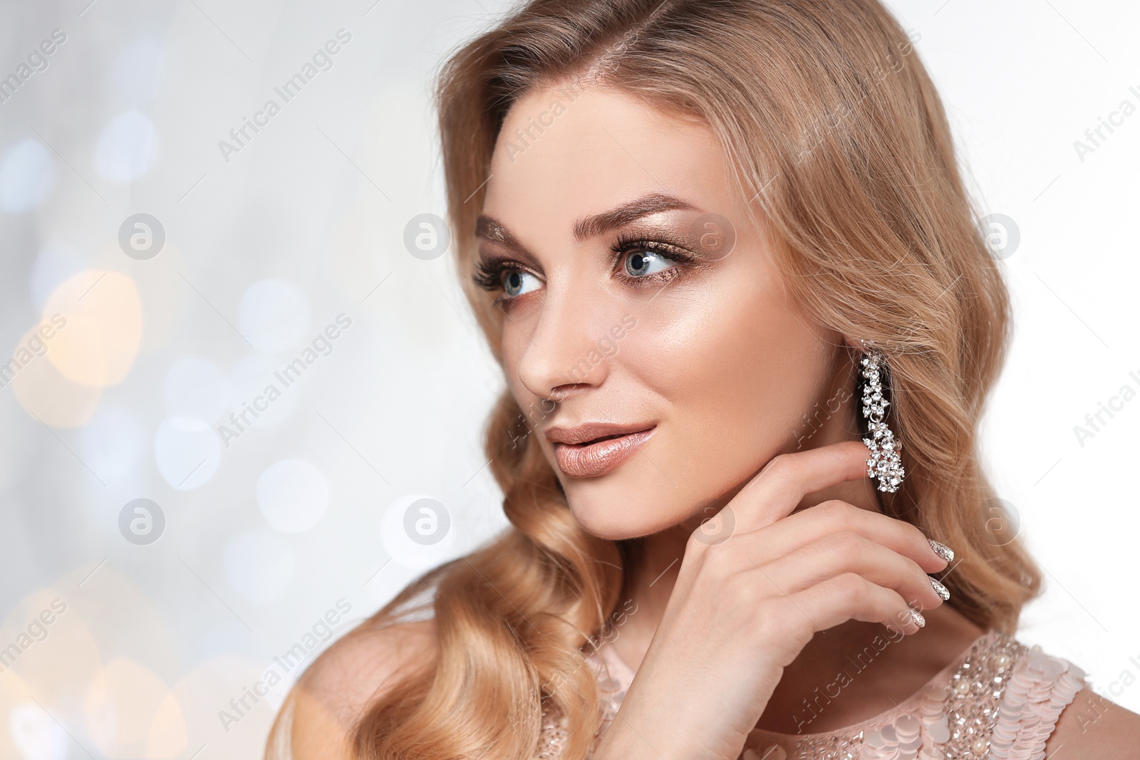 Photo of Beautiful young woman with elegant jewelry against defocused lights. Space for text