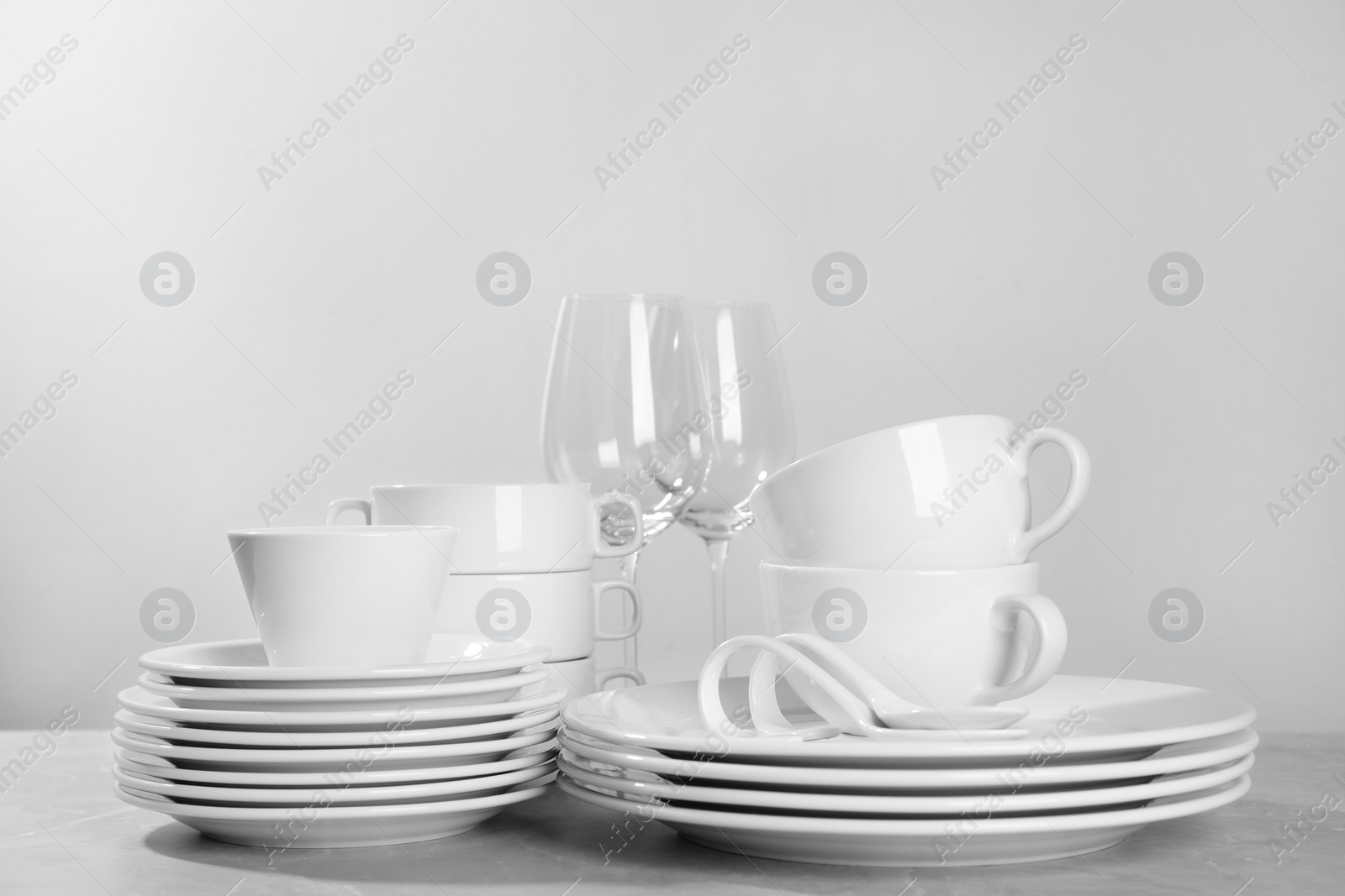 Photo of Set of clean dishware and glasses on grey table against light background