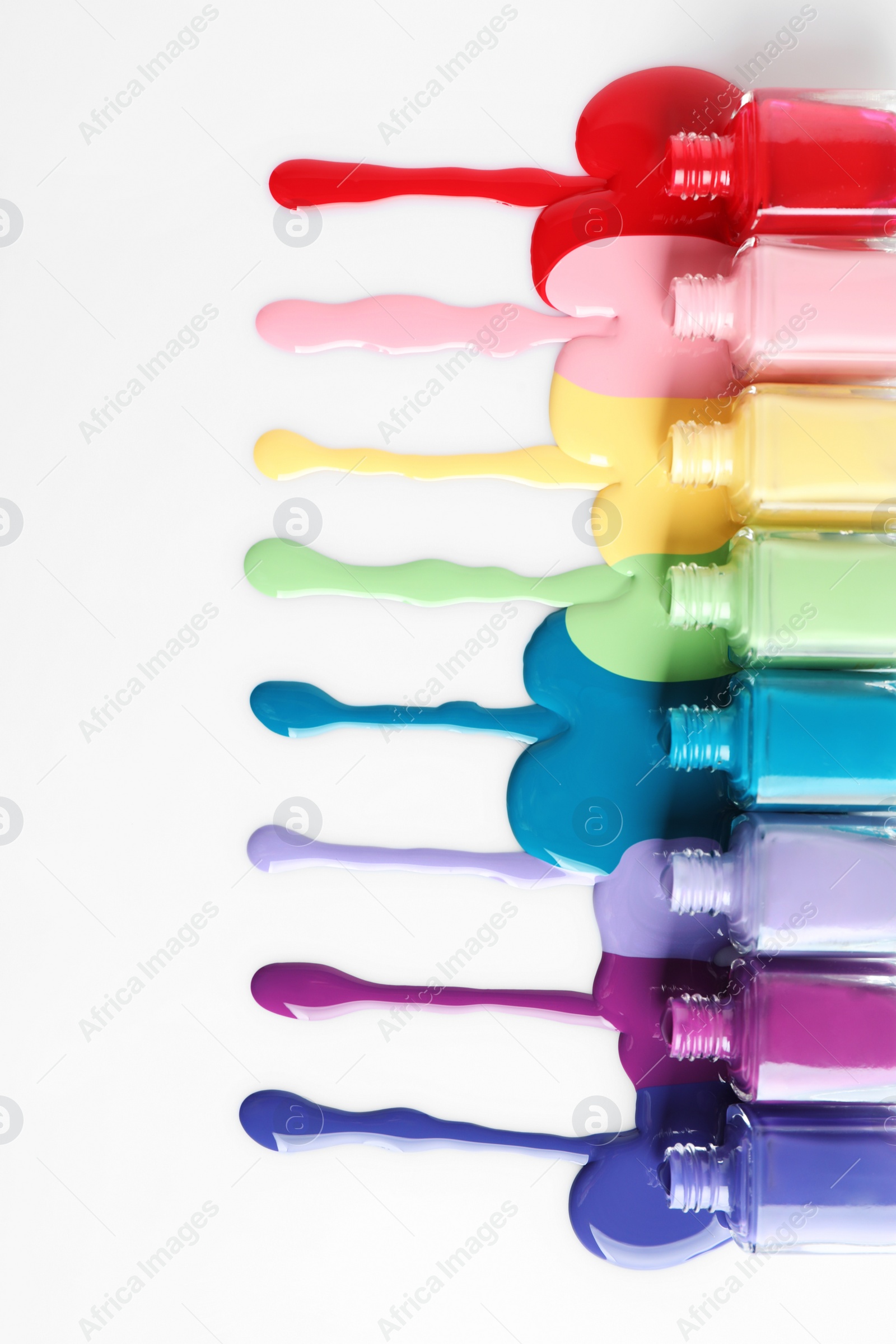 Photo of Spilled colorful nail polishes and bottles on white background, top view