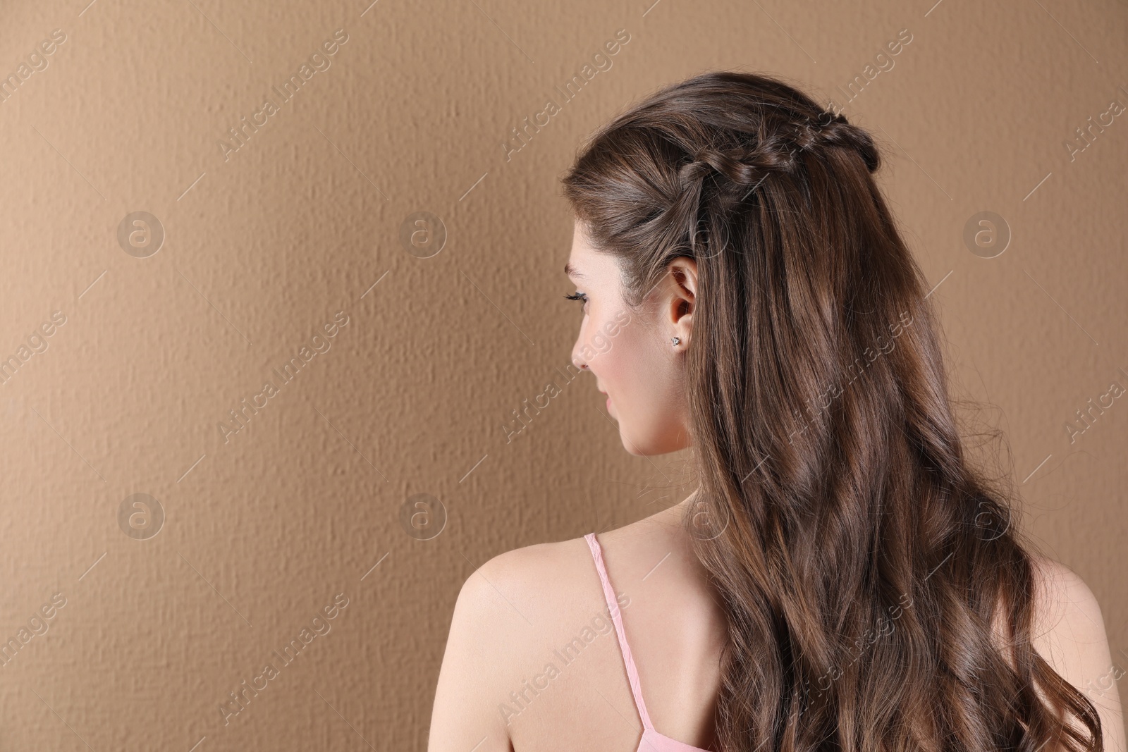 Photo of Woman with braided hair on light brown background, back view. Space for text