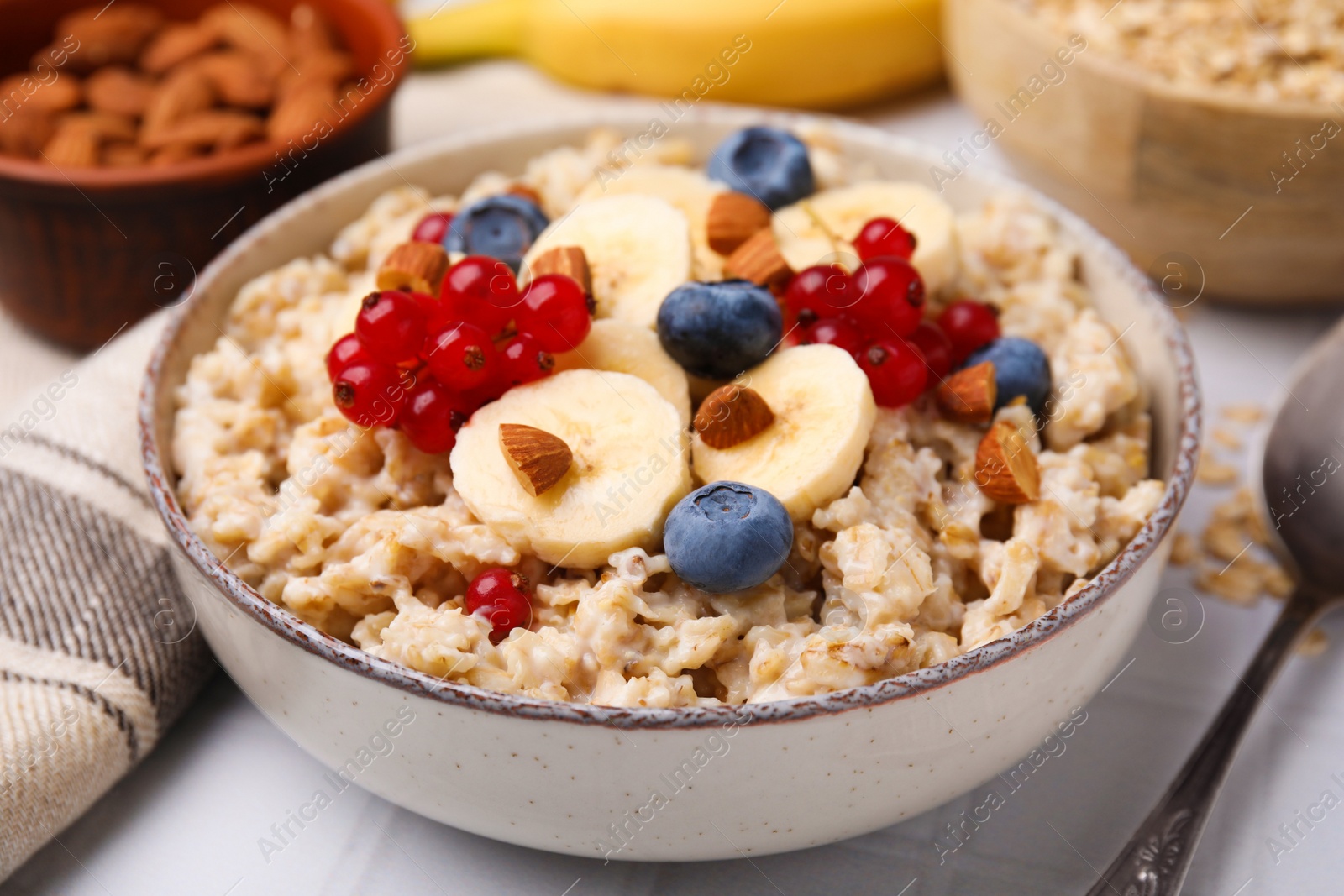 Photo of Oatmeal served with berries, almonds and banana slices on white table, closeup