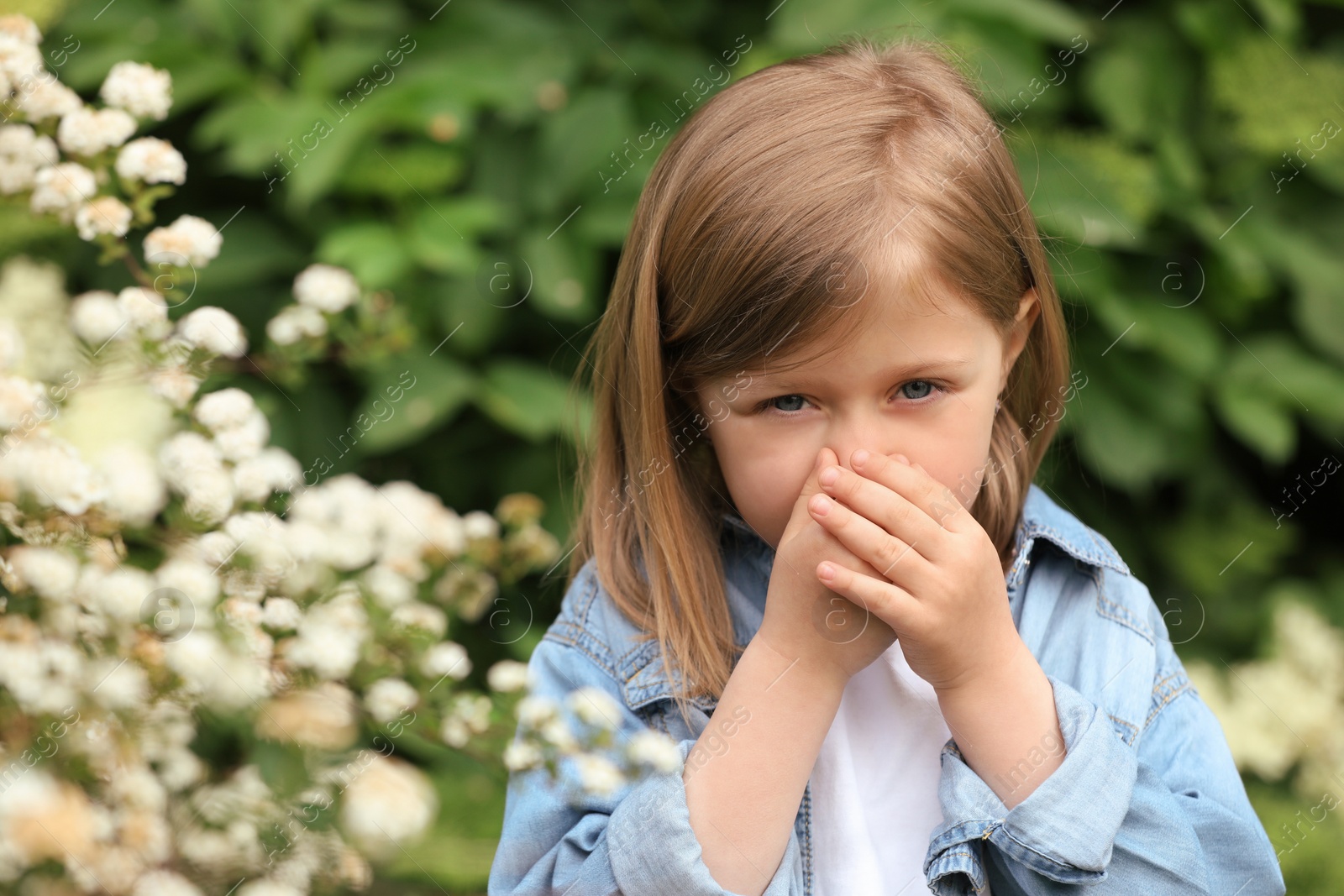 Photo of Little girl suffering from seasonal pollen allergy near blossoming tree on spring day