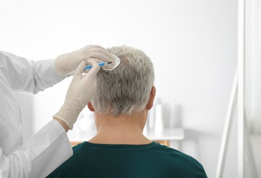 Photo of Senior man with hair loss problem receiving injection in salon